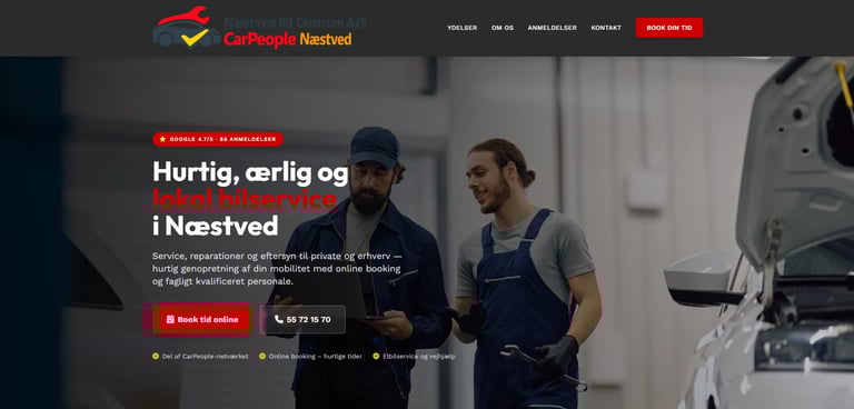 Two car mechanics in work uniforms discussing repairs next to an open hood of a vehicle